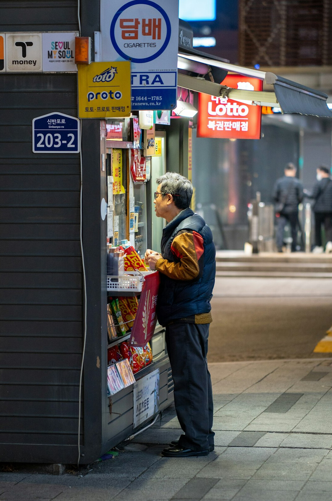 Middle-aged Latino shopkeeper closing the metal shutters of a corner store at dusk