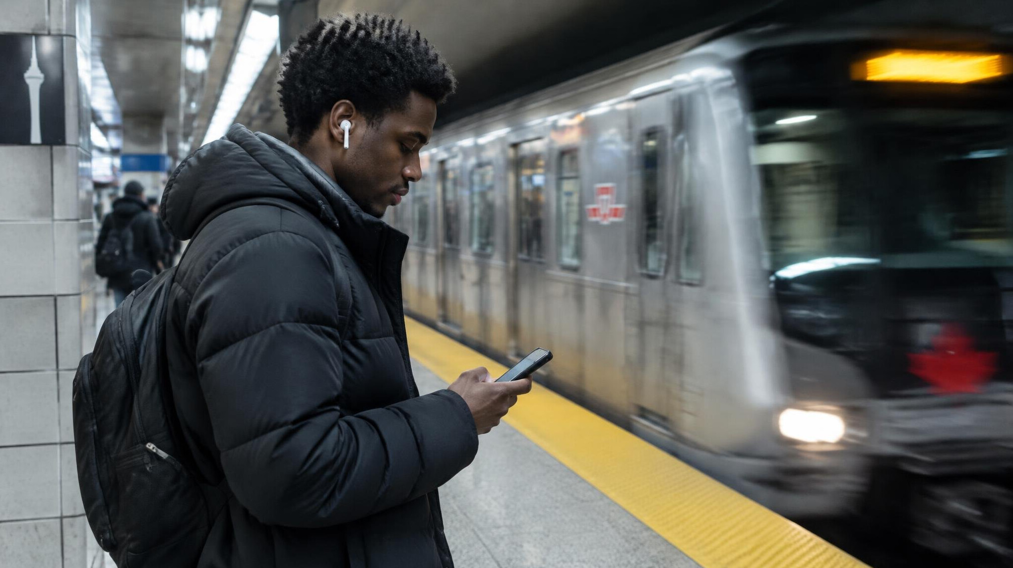 Young Black man checking his phone while waiting on a city subway platform